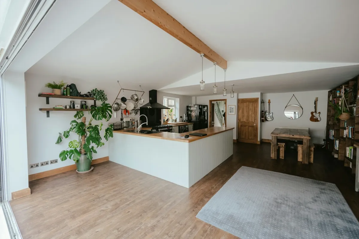 Open-plan kitchen with laminate worktops on white handleless cabinets, exposed oak beam and open shelving with plants