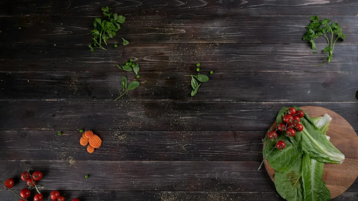 Dark stained solid wood worktop surface with fresh herbs, cherry tomatoes and a chopping board ready for food preparation