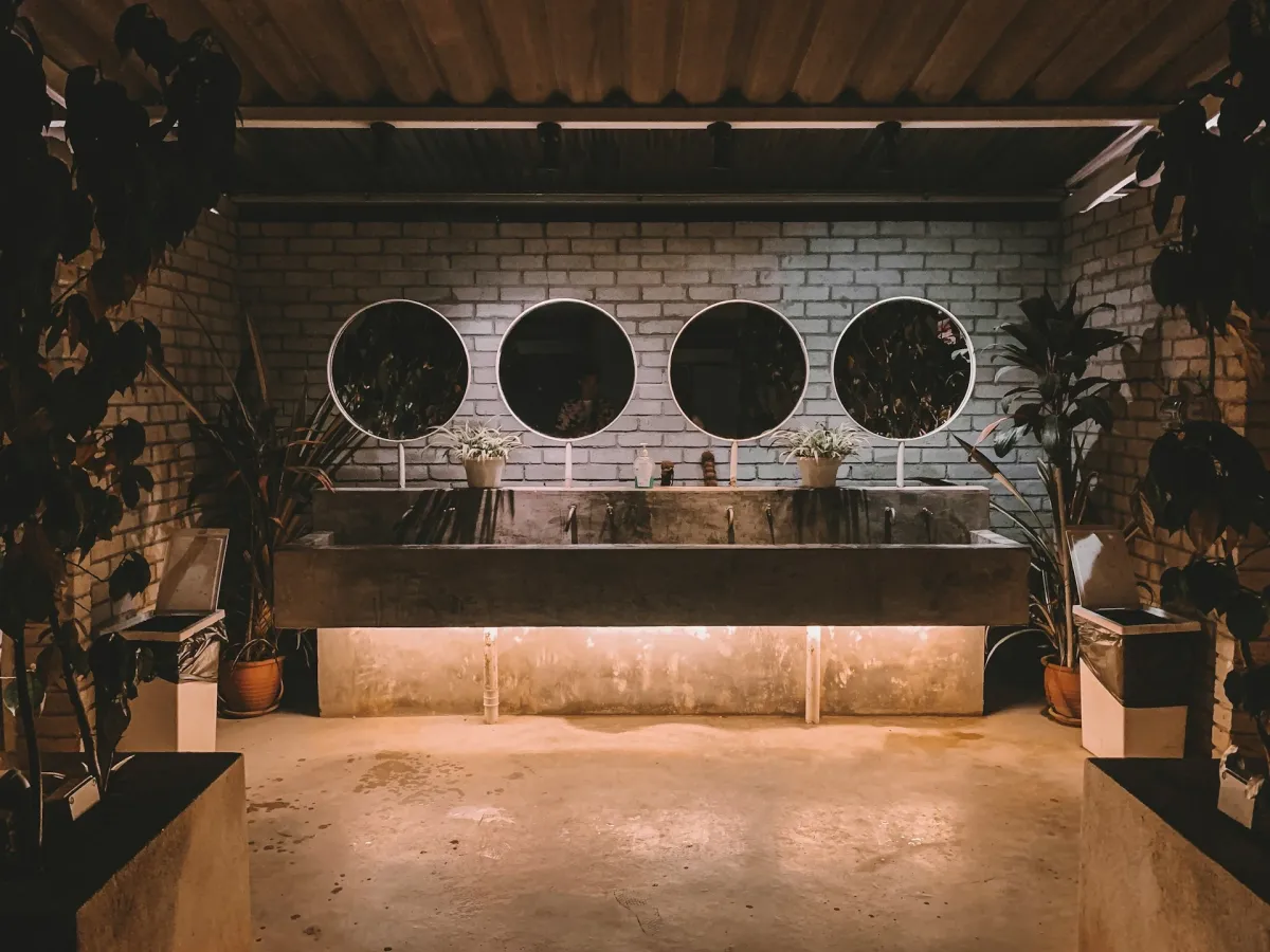 Four round backlit mirrors mounted on a white brick wall above a concrete vanity with ambient under-counter lighting