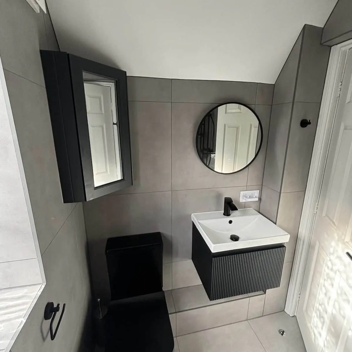 Small Didsbury en-suite under a sloping ceiling with matt black toilet, fluted black vanity, and round mirror