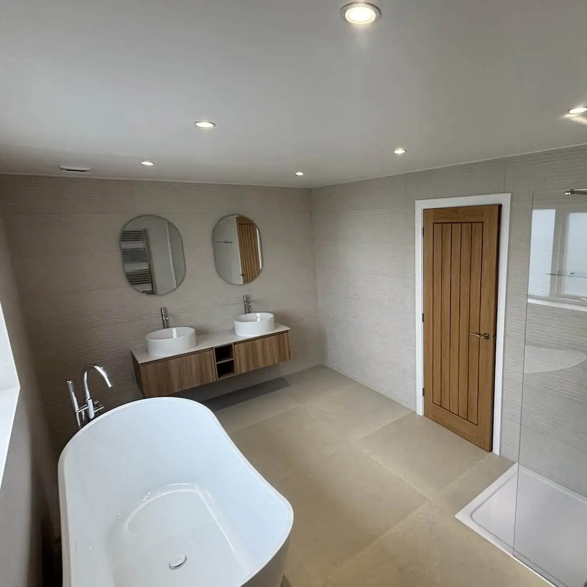 Wall-hung oak-look double vanity with two vessel basins beside a freestanding bath in a Poynton bathroom