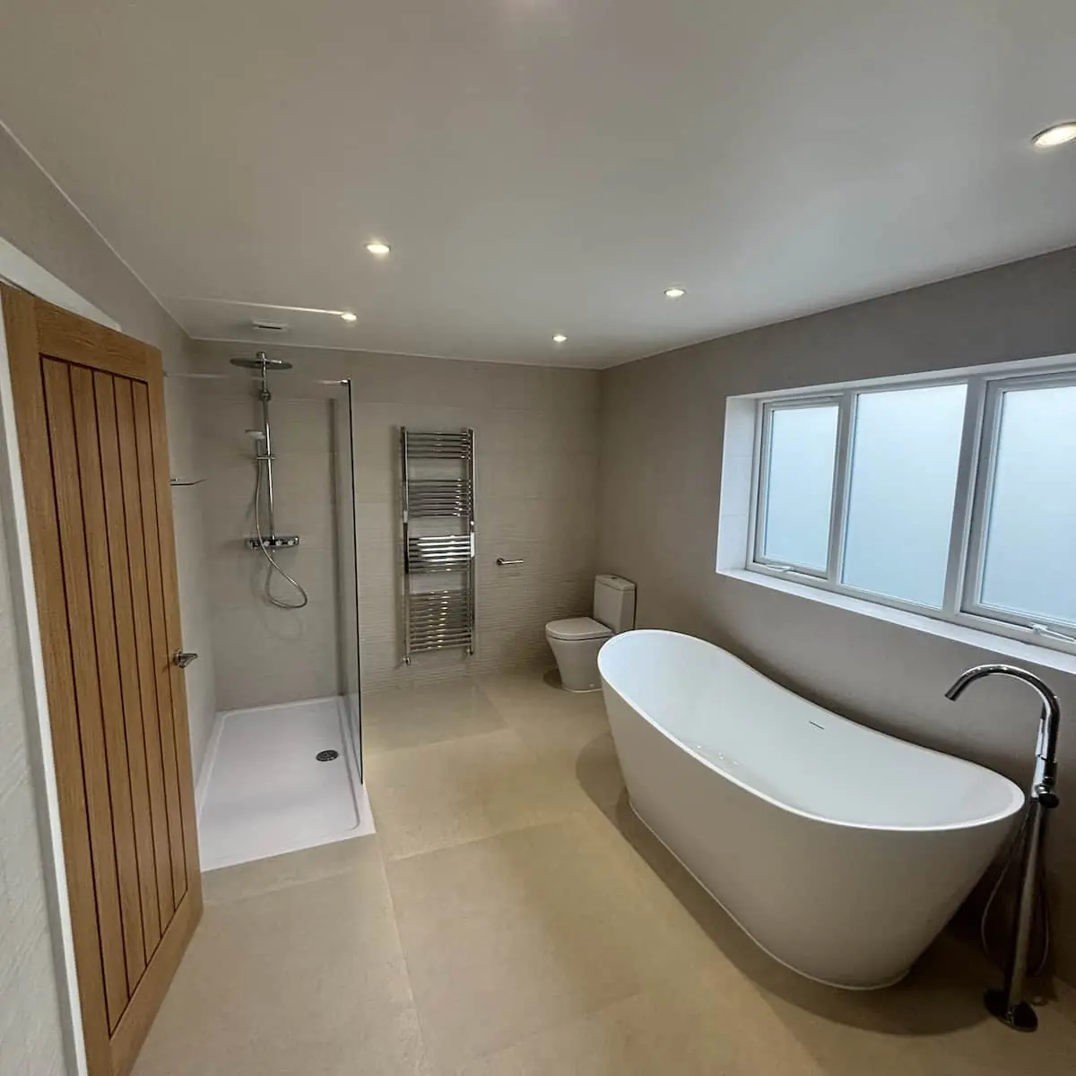 Poynton bathroom with a freestanding bath, walk-in shower, oak-look door, and large stone-effect floor tiles