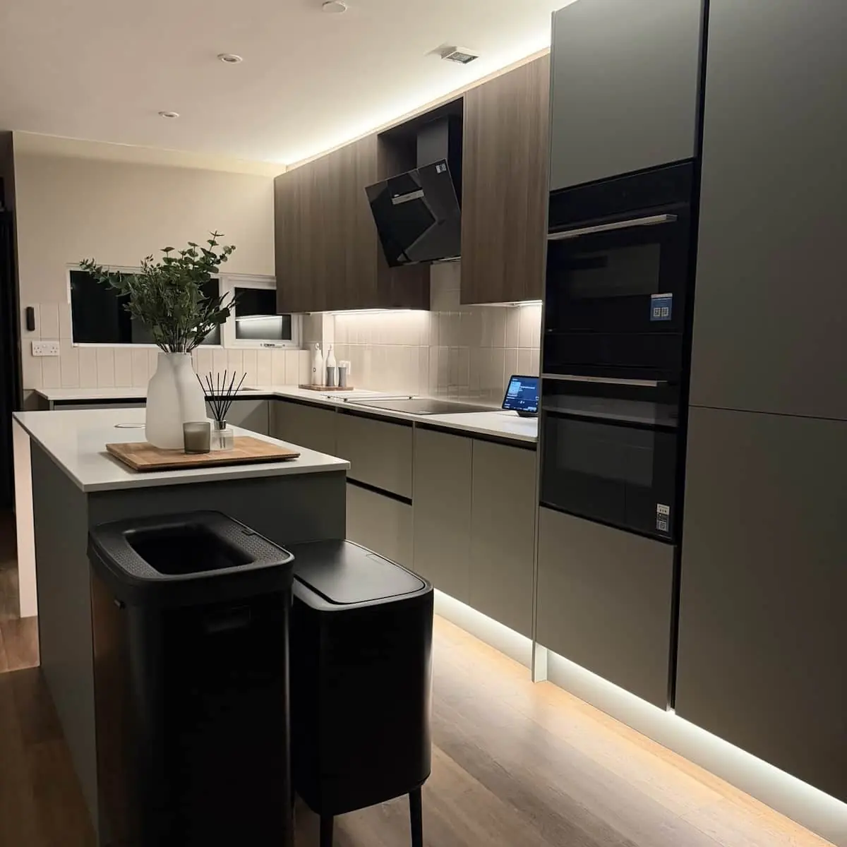 Evening view of a supplied and fitted handleless kitchen with stacked built-in appliances and LED plinth lighting