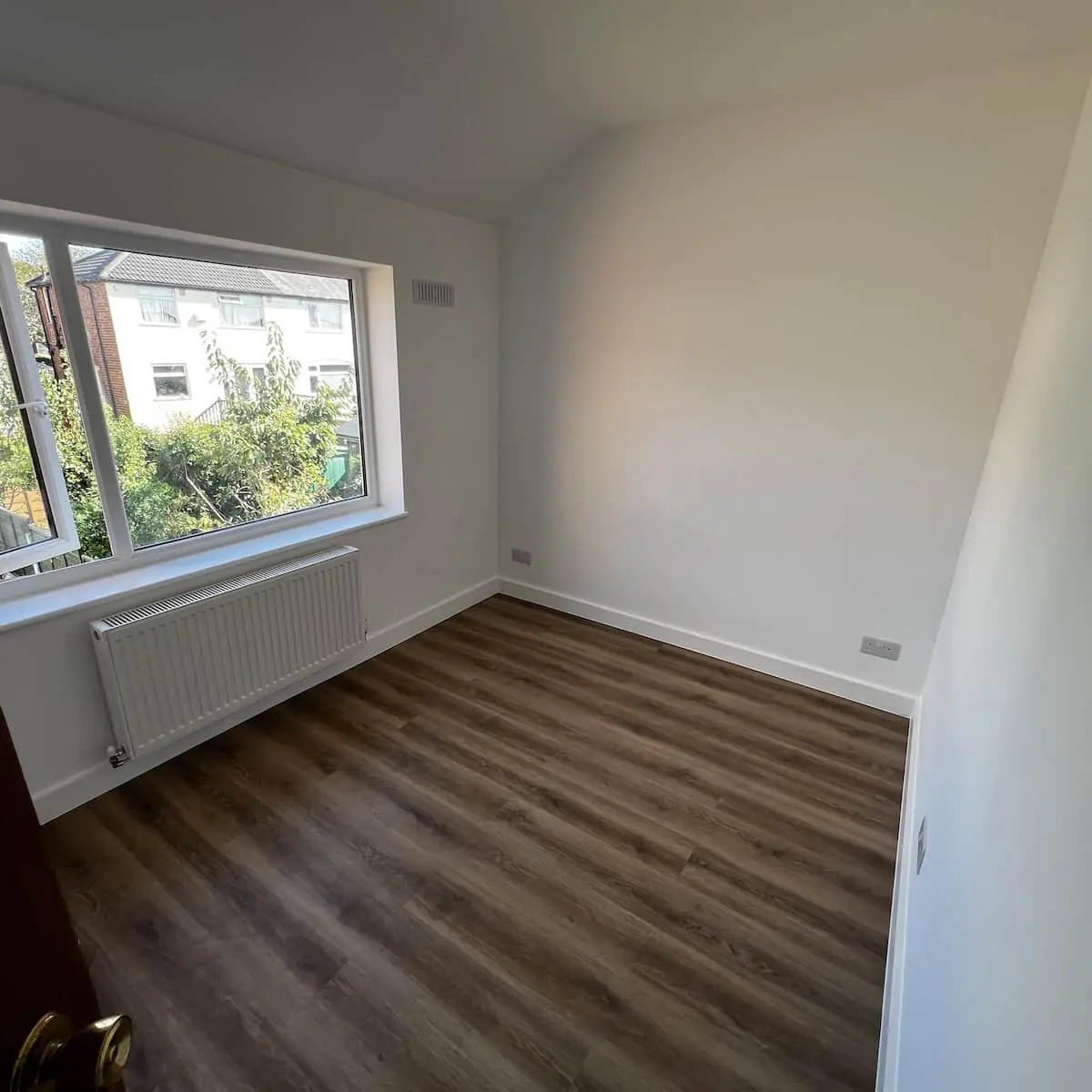 Freshly plastered and painted room with new skirting, radiator, and wood-effect flooring