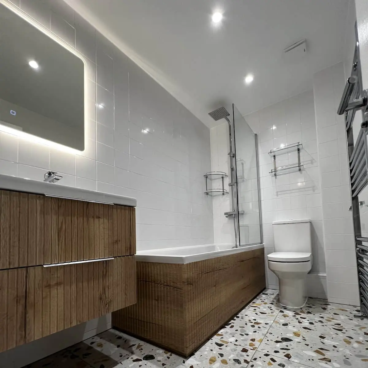 Didsbury main bathroom with terrazzo-look floor, oak-look fluted vanity and bath panel, and an LED mirror
